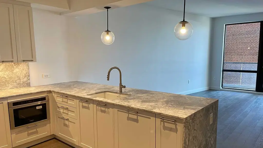 Finished kitchen in a renovated New York apartment with white cabinets, a stone countertop and pendant lights